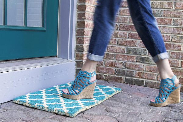 A teal doormat with a crosscross white Moroccon style print with a woman in heels walking across it.