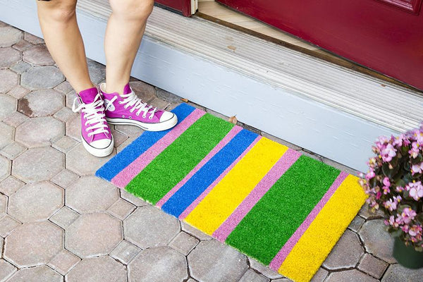 Coir doormat with yellow, blue, pink and green stripes outside door.