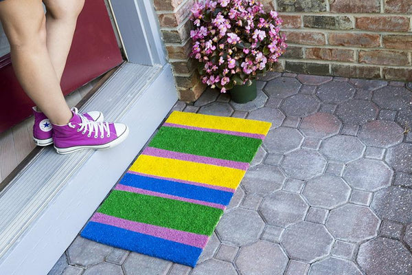 Coir doormat with yellow, blue, pink and green stripes outside door.